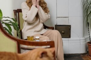 A woman sneezing in a cozy interior with a ginger cat and houseplants, depicting allergy season.