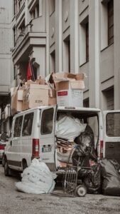 A white van loaded with cardboard boxes and bags in a crowded alleyway, illustrating urban storage challenges.